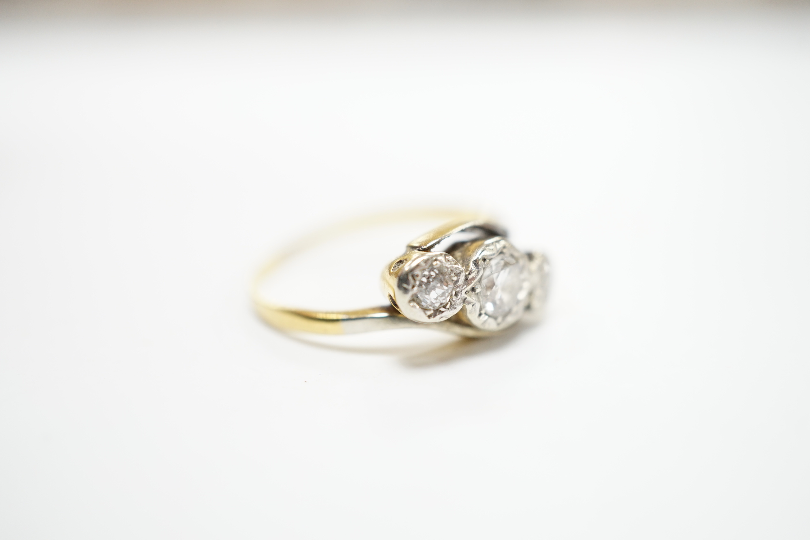 A yellow metal and illusion set three stone diamond set crossover ring, size O/P, gross weight 3.2 grams.